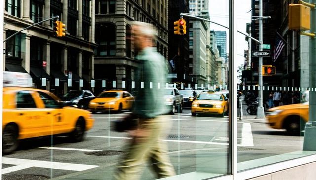 Blurred pedestrian crossing reflecting yellow taxis on downtown glass facade