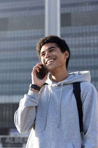 African american teen talking on phone in urban daylight wearing hoodie and backpack