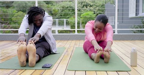 African American friends stretching together on balcony yoga mats practicing flexibility