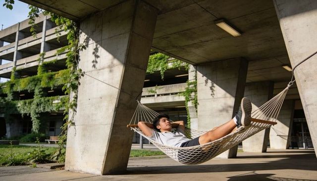 Young man relaxing in hammock under concrete canopy with urban greenery