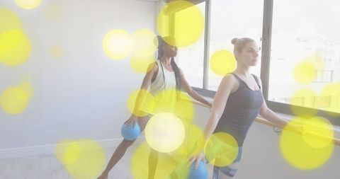 Two women practicing barre fitness with exercise balls in studio for balance and mobility