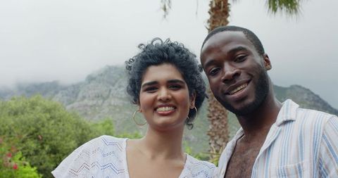 Smiling multicultural couple enjoying mountain getaway with palm tree and overcast sky