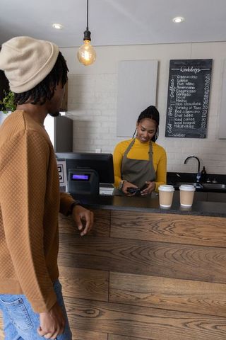 African american barista processing card payment at wood counter in cozy coffeehouse
