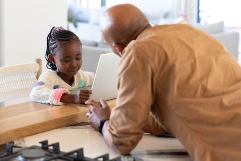 African american father helping daughter with online learning at kitchen counter