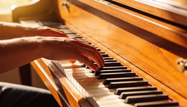 Warm sunlit hands playing upright piano keys in cozy wood interior for practice and relaxation