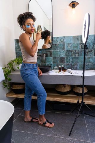 African american woman applying hydrogel eye patches at vanity with ring light