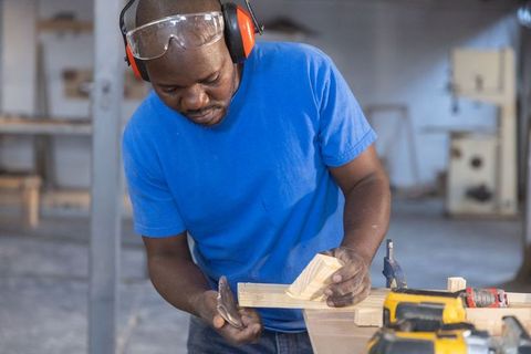 Senior african american man measuring wood block in woodshop, focused carpenter at work