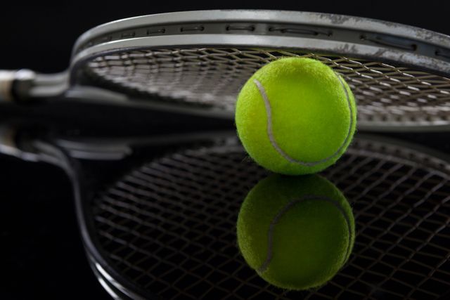 Close up of racket on fluorescent yellow tennis ball with reflection against black background