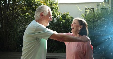 Laughing senior couple embracing in sunlit backyard garden, conveying joy and affection