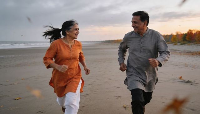 Senior indian couple running along beach at sunset embracing active healthy retirement
