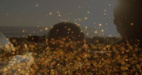 Backlit mother cradling infant by roadside at dusk with warm golden bokeh and silhouette