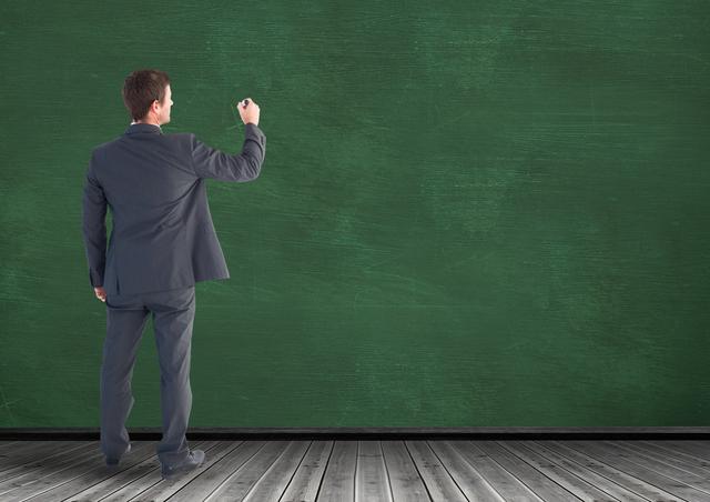 Businessman in a formal suit writing on a large green chalkboard, positioned in an indoor setting with wooden flooring. Useful for illustrating corporate training, educational presentations, professional development sessions, or business coaching scenarios.