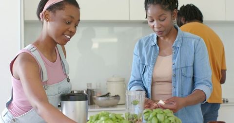African family preparing herb smoothie in modern kitchen, mother and daughter collaborating
