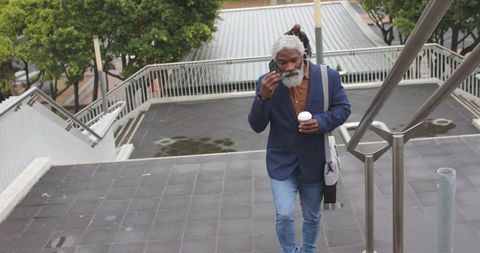 Mature african american professional climbing stairs holding coffee and adjusting earbud