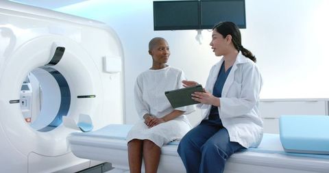 Clinician consulting female patient beside ct scanner in modern radiology clinic