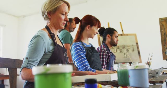 Group of adults from diverse backgrounds concentrating on painting during an art class. Ideal for use in contexts involving learning, creativity, community activities, or any artistic endeavor imagery.