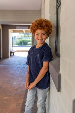 Smiling african american boy leaning against brick wall in sunlit passageway