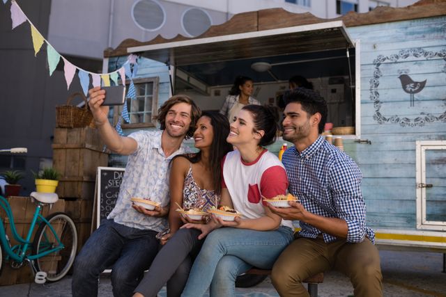 Group of friends enjoying their time together taking a selfie near a food truck. Ideal for use in advertisements or social media posts about friendship, outdoor activities, and street food culture.