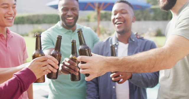 Happy diverse male friends talking and drinking beer in garden on sunny day. spending quality time outdoors together.