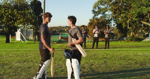 Young cricket players congratulating and chatting after match on sunlit park outfield