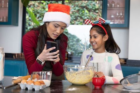 Asian mom and daughter baking treats, checking smartphone recipe, stirring batter