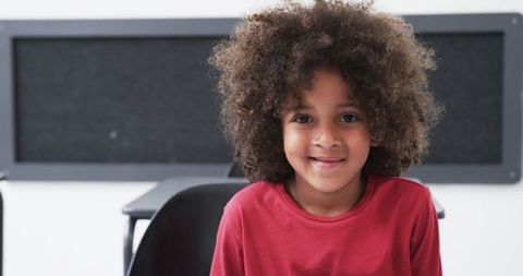 Smiling Young Boy in Classroom with Curly Hair and Red Shirt