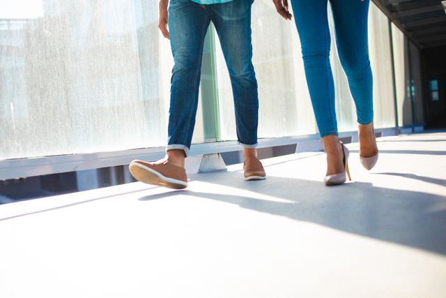 Low section of businessman and businesswoman wearing blue jeans walking in office corridor. unaltered, business, corporate business, occupation and office concept.