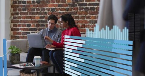 Colleagues collaborating on laptop with animated data charts in modern office lounge