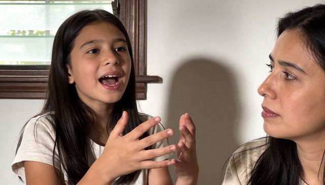 Preteen girl talking and gesturing, mother listening in home interior