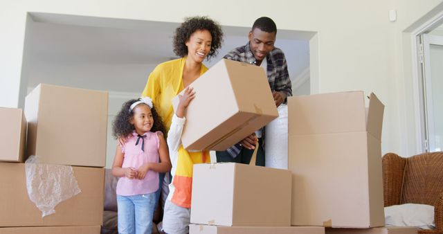 An African American family is happily moving into a new home, holding and carrying cardboard boxes while smiling. This can be used for themes related to family relocation, new beginnings, home purchase, and real estate.