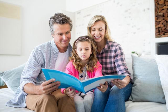 Family sitting on couch in living room, looking at photo album together. Parents and child sharing memories, creating a warm and loving atmosphere. Ideal for use in articles about family bonding, home life, parenting tips, and creating lasting memories.