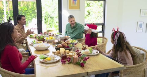 Diverse family enjoying festive holiday meal around wooden dining table with roast turkey