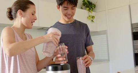 Young couple making berry smoothies in bright modern minimal white kitchen
