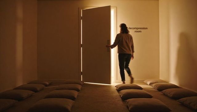 Woman walking toward open door of decompression room in minimalist calm interior