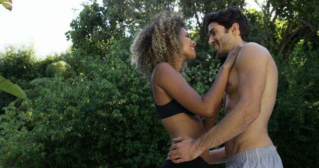 A young biracial woman and a young Caucasian man share a romantic moment outdoors, with copy space. Their affectionate gaze and smiles suggest a deep connection and happiness in each other's company.