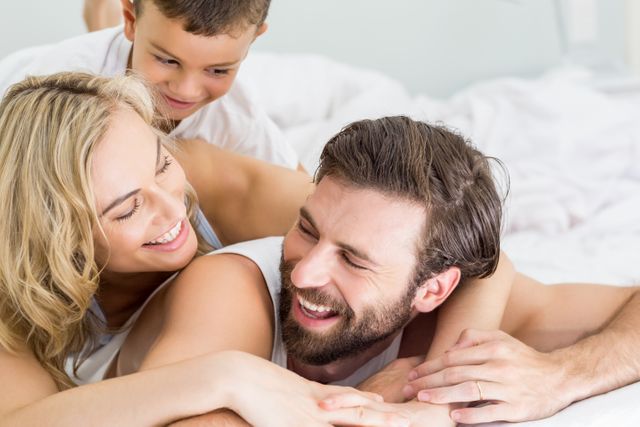 Parents and son lying on bed and having fun at home