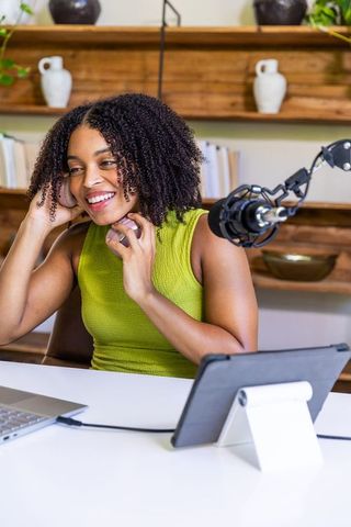 Smiling african american podcaster adjusting headphones in modern home studio recording