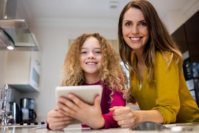 Mother and daughter using digital tablet in kitchen at home