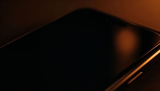 Smartphone reflecting warm amber glow on dark tabletop, curved glass and side button