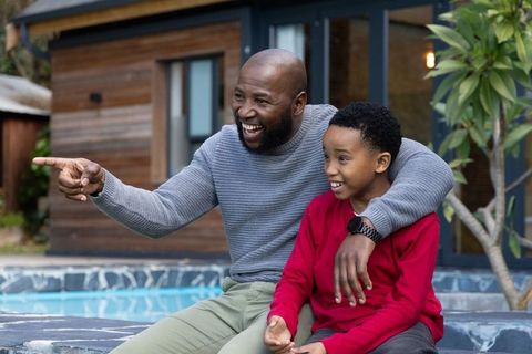 African american father laughing and pointing with son on backyard pool patio