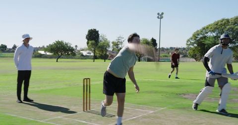 African american bowler delivering while batsman retreating on sunny cricket pitch