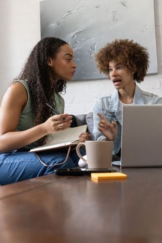 African american women collaborating on laptop and notebook discussing creative project
