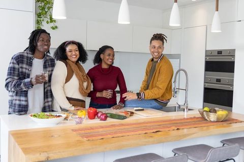 African American Friends Chatting and Preparing Fresh Salad on Wooden Kitchen Island with Veggies