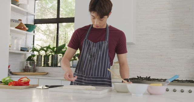 Asian male teenager preparing food and wearing apron in kitchen. spending time alone at home.