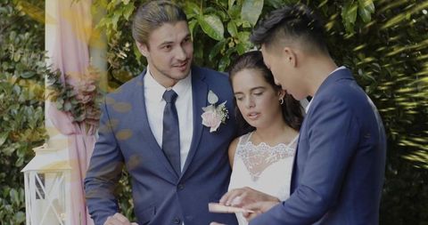 Checking wedding details: groom and best man supporting bride during outdoor ceremony