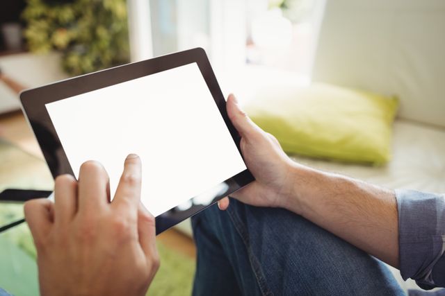 Man using digital tablet while relaxing on sofa in living room. Ideal for illustrating concepts of modern technology, home leisure, casual lifestyle, and wireless internet browsing. Suitable for use in articles, blogs, advertisements, and websites related to technology, home living, and digital devices.