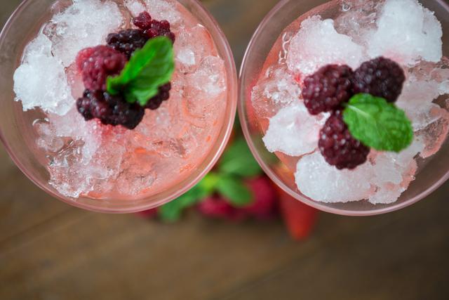 Overhead view of a refreshing strawberry cocktail garnished with fresh mint leaves and crushed ice. Ideal for use in summer beverage promotions, cocktail recipes, party invitations, and food and drink blogs.