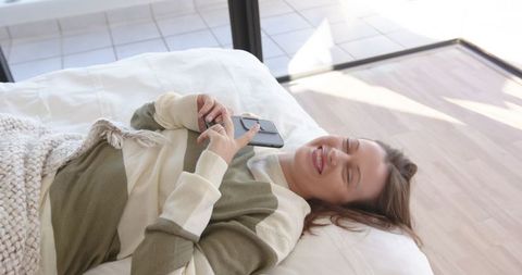 Woman Relaxing on Bed Holding Smartphone in Modern Interior
