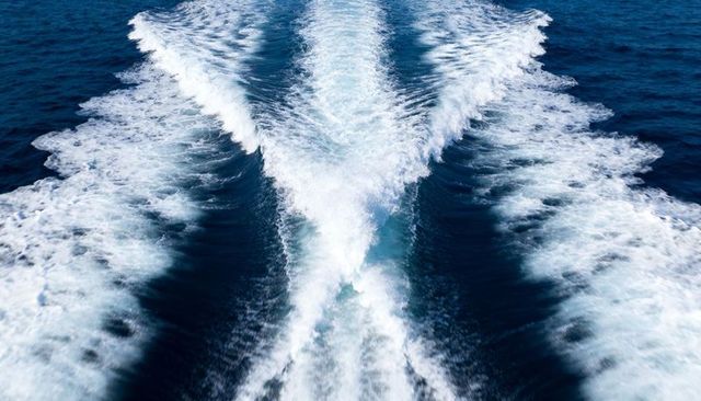 V-shaped boat wake cutting through deep blue ocean with foamy turbulent trails and ripples