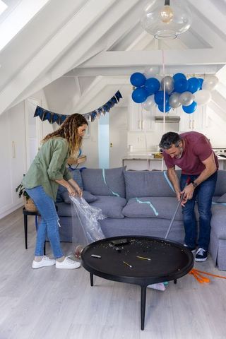 Couple cleaning up after birthday party in modern vaulted living room with gray sofa and balloons